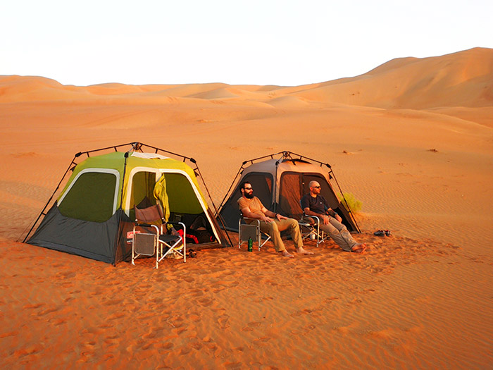 campo tendato mobile montato nel deserto del Rub Al Khali con viaggiatori che si godono il tramonto che annuncia la notte